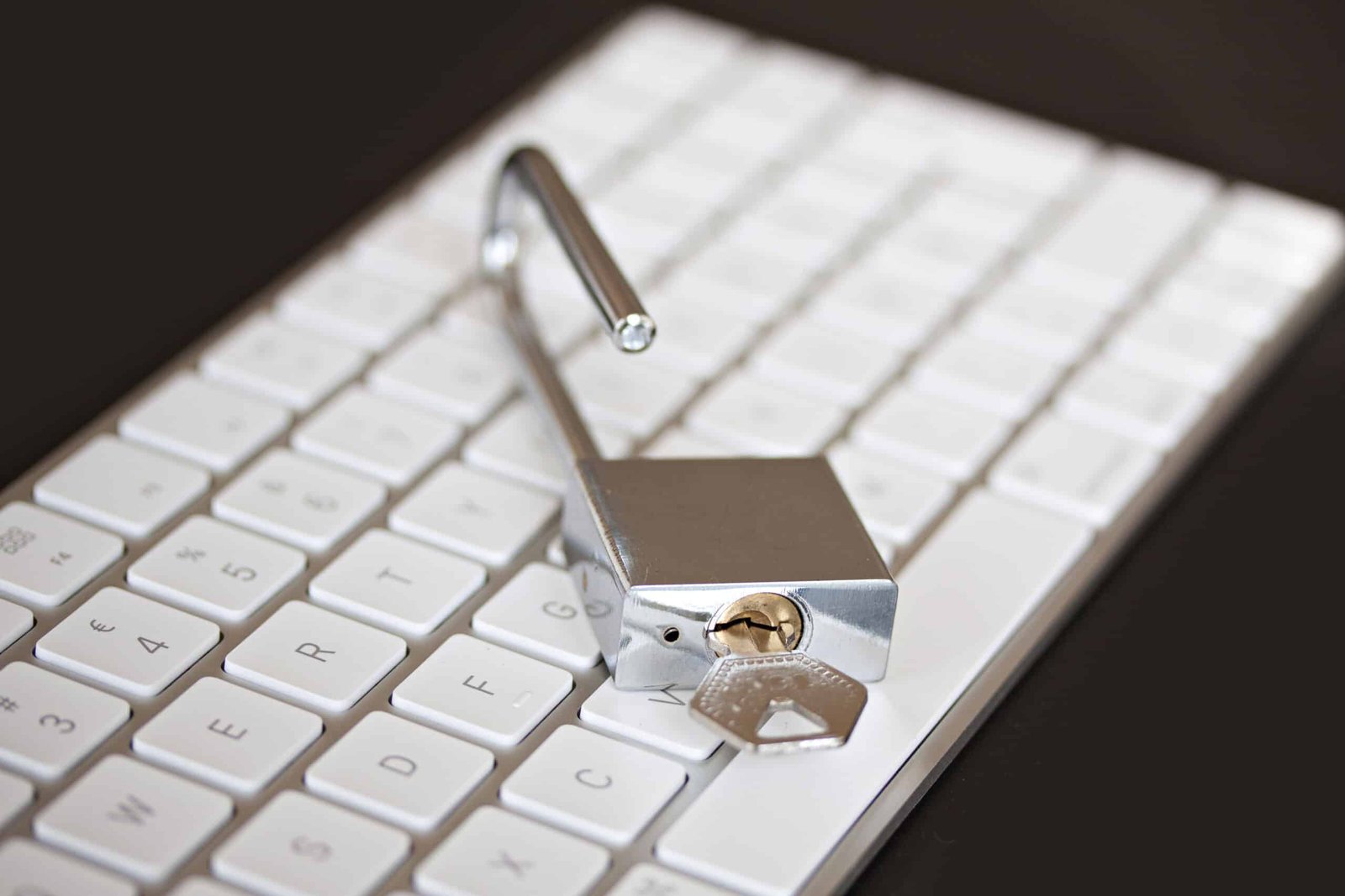 Unlocked silver padlock with key on white computer keyboard