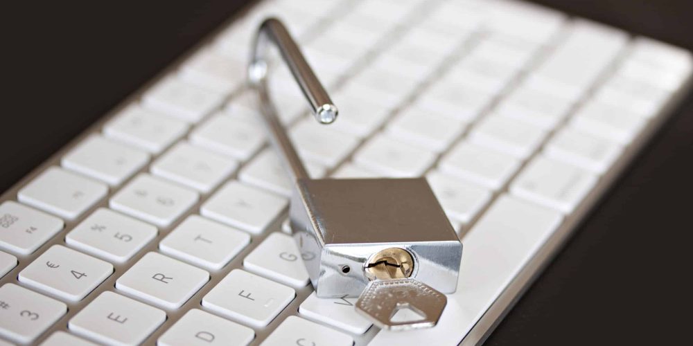 Unlocked silver padlock with key on white computer keyboard